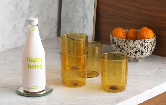 Kitchen counter with yellow glasses and a bottle of happy being cucumber mint